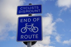 Sign showing End Of Route for cyclists.  Blue road sign under blue cloudy sky. Cyclists Dismount signpost.