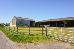 Roadside view of various farm buildings. Barn and shelters at farmyard in UK. Countryside scene on sunny day.