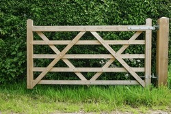 A wooden gate in open position next to hedge of rural garden 