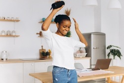 Young black woman dancing in the kitchen holding a bluetooth speaker