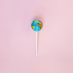 Globe lollipop on pastel light pink background. Minimalistic environment composition. Creative candy world flat lay. Beauty of the planet idea. World Earth day concept.