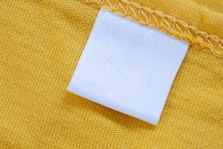 White blank clothing tag label on new yellow shirt background