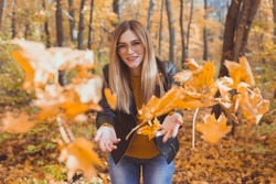 Happy laughing young woman throwing leaves in autumn park. Fall season