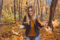 Happy laughing young woman throwing leaves in autumn park. Fall season