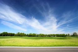 Green meadow and blue sky with asphalt road on foreground. Landscape in summer sunny day. 