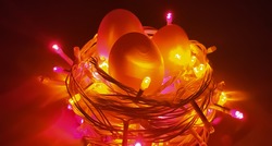 Artistic creative conceptual photo design of Easter eggs in bird nest made with colorful glowing decoration led light bulbs and electric wire on dark black background and copy space. Close up top view