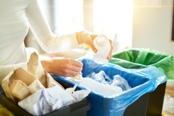 Woman putting empty plastic bottle in recycling bin in the kitchen. Person in the house kitchen separating waste. Different trash can with colorful garbage bags.