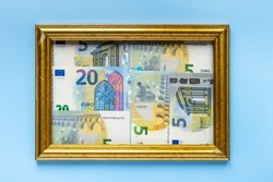 euro money in denominations of 20 euros and 5 euros in a golden photo frame on a blue background