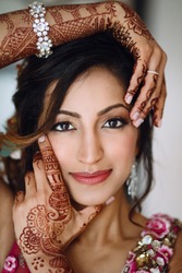 Portrait of beautiful Hindu bride holding hands with henna tattoos before her face
