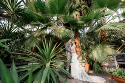 Front view of beautiful newlyweds stand and hug among palm trees. Concept of wedding couple