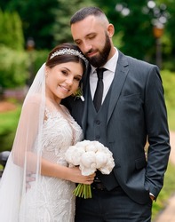 Portrait of happy married couple, wearing in vogue wedding outfits, standing together outdoor, smiling and posing at camera during wedding day