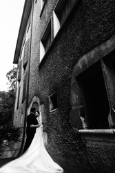 Sunlit romantic married couple on bridge with flowers leaning against old wall b&w