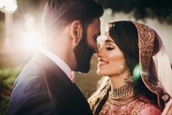 Handsome bearded Indian groom kisses bride in pink dress tender standing outisde