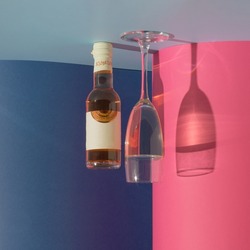 A creative gravity illusion with a bottle and a glass on a blue and pink background. Minimal party and drink concept. Socializing and New Year inspiration.