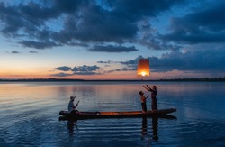 Fisherman family are flying lantern on the boat in the lake at sunset