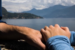 Couple. You can see the hands touching each other. Sensually.Water and mountains in the background.