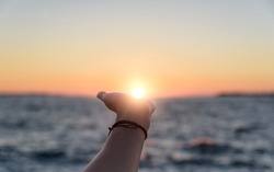 Female hand reaches for the sun at sunset against the background of the sea.