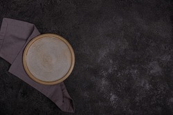 An empty beige ceramic plate on a dark black background. Grey linen napkin. Copyspace