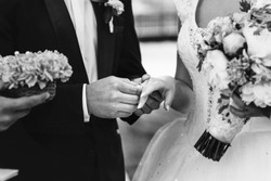 Black and white groom and beautiful bride exchanging wedding rings closeup