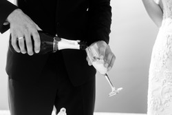 Groom opening champagne at wedding aisle tent sea background closeup b&w