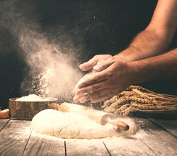 Man preparing bread dough on wooden table in a bakery close up