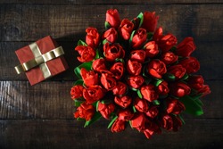 Top view bouquet of red tulips with red gift box on dark wooden table with copy space