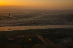 Hot air balloons at sunrise above Luxor, Egypt. The city is covered in thick morning fog.