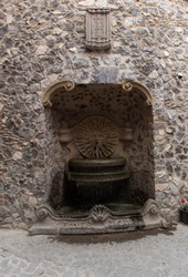 stone fountain with a spitting sun with face and the inscription 