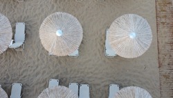 Aerial view of rows of cane umbrellas and sunbeds on a sandy Mediterranean beach