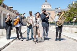 Jazz band playing in the street in broad daylight and dressed with jackets, caps and dresses; composed of 6 components, a singer, a clarinet, a tuba, a trombone, a guitar and a washboard. 