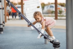 Toddler 1-2 years old girl on the playground with a cast on her arm to climb high on a rope net or web in an outdoor playground. Get injured while playing on the court. Safety engineering
