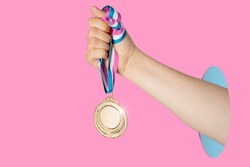 Hand of woman holding gold medal on pink background.award and victory concept.copy space