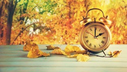  Clock and leaves on wooden table.