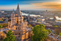 Budapest, Hungary - Beautiful golden summer sunrise with the tower of Fisherman's Bastion and green trees. Parliament of Hungary and River Danube at background. Blue sky.
