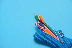 Funny Back to School concept - pencil case eating pencils on blue background. Space for text.