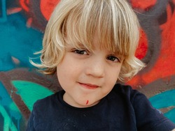 Portrait of a cute blonde caucasian child with stained face after been painting a graffiti 