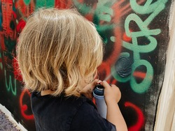 Caucasian three years old child painting graffiti on a wall at the street with a black t-shirt