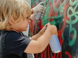 Caucasian three years old blonde child painting graffiti with a spray at the wall with effort face