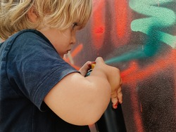 Caucasian three years old child painting graffiti on a wall at the street with a black t-shirt for the first time
