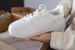 Unpacking women's shoes, stylish white sneakers in hands.