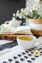 Cup of chamomile tea, open book, wicker basket with flowers, atmospheric photo
