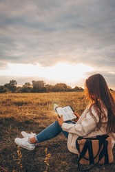 Christian woman holds bible in her hands. Reading the Holy Bible in a field during beautiful sunset. Concept for faith, spirituality and religion. Peace, hope
