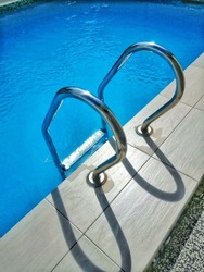 grab bars ladder in a blue water swimming pool. steel ladder at pool.