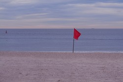 Warning sign of a red flag at a beautiful beach with a blue cloudy sky in New Jersey USA