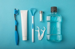 Toothbrush, tongue cleaner, floss, toothpaste tube and mouthwash on blue background with copy space. Flat lay. Dental hygiene. Oral care kit. Dentist concept.