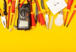 Electrician tools on yellow background.Multimeter,construction tape,electrical tape, screwdrivers,pliers,an automatic insulation stripper, socket and LED lamp.Flatley.electrician concept.