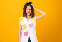 Boring young Asian woman hand touching on head and a sticky note on the clothes, stand on studio shot yellow background.