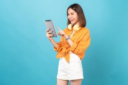 Cheerful young Asian woman in headphones listening to music and enjoy favourite playlist application on digital tablet with dancing on blue background.