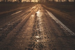 dirty sand and gravel road with puddles in sunset golden light