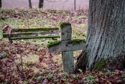 old aged moss covered wooden cross and old bench on grave site in abandoned Latvia cemetery